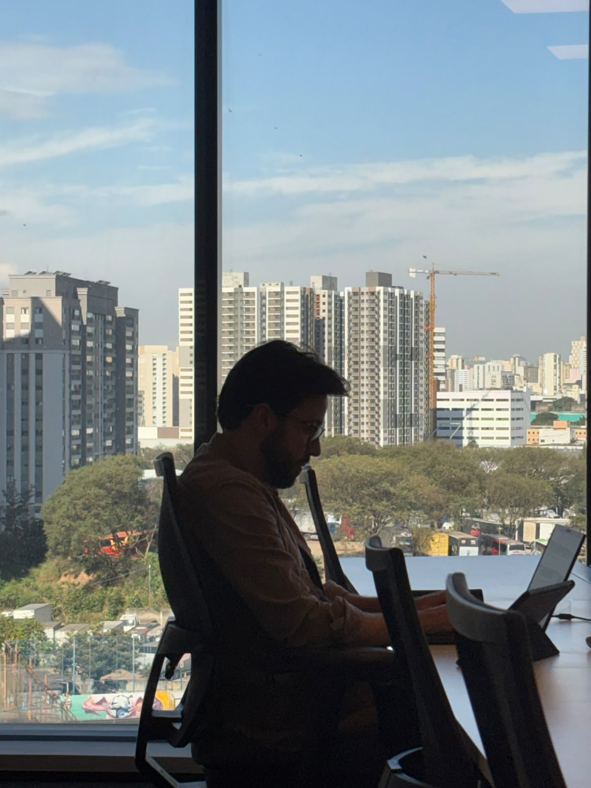 Profissional trabalhando no notebook diante de uma janela ampla com vista para a cidade